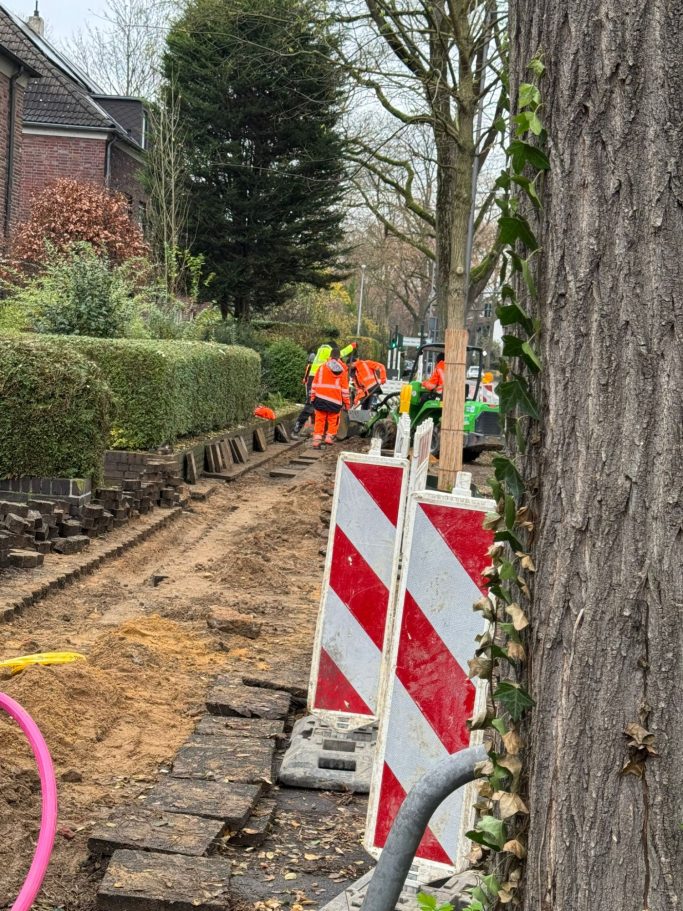 Bauarbeiten mit Arbeiter in orangefarbener Kleidung und Absperrungen in einer Straße.
