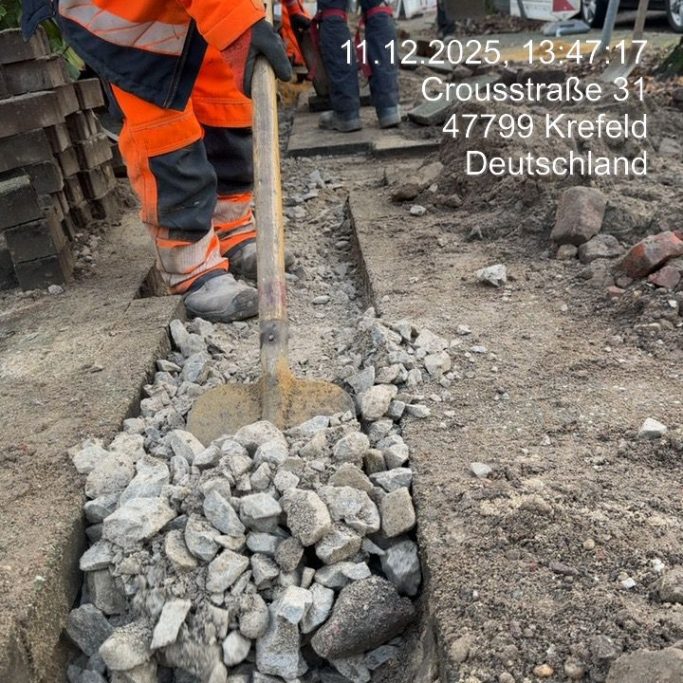 Mitarbeiter gräbt mit einer Schaufel einen Schotterweg in einer Baustelle.