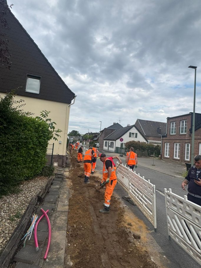 Arbeiter in orangefarbener Kleidung graben entlang einer Straße. Häusliche Umgebung.