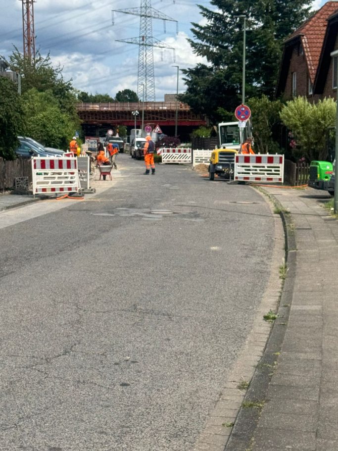 Bauarbeiten auf der Straße mit Absperrungen und Arbeiter in orangefarbener Kleidung.