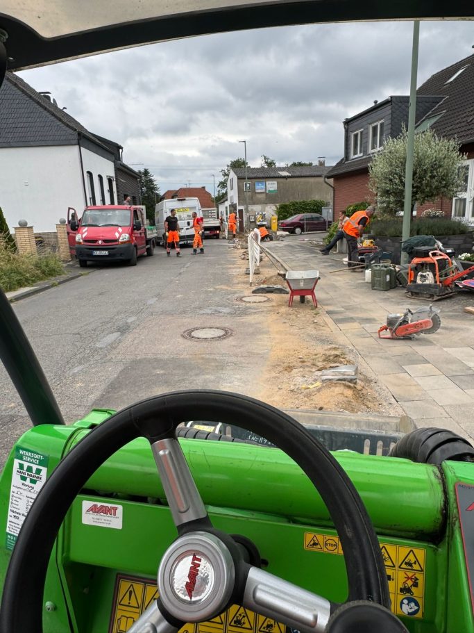 Blick von einem Traktor auf eine Baustelle mit Bauarbeitern und Fahrzeugen.