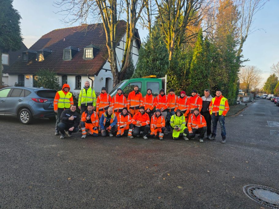 Gruppe von Personen in orangefarbenen Sicherheitswesten, versammelt auf der Straße.