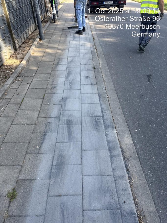 Grau gepflasterter Gehweg mit Fußgänger und Absperrung auf der Seite.