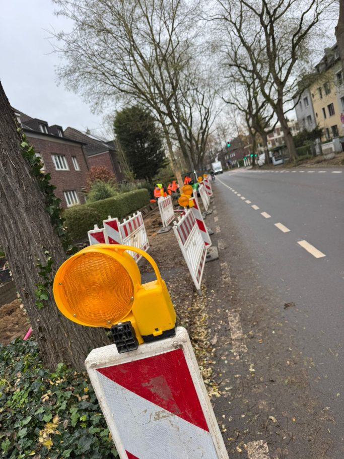 Bauarbeiten am Straßenrand mit leuchtenden Warnleuchten und Baustellenschildern.