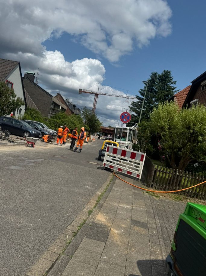Bauarbeiten auf einer Straße mit Arbeitern in orangefarbener Kleidung und Absperrungen.