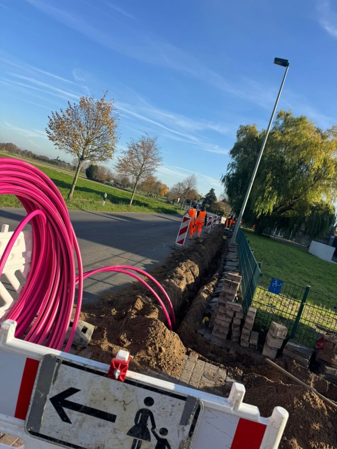 Bauarbeiten an einer Straße mit Kabeln, Absperrungen und Arbeitsschutzkleidung.