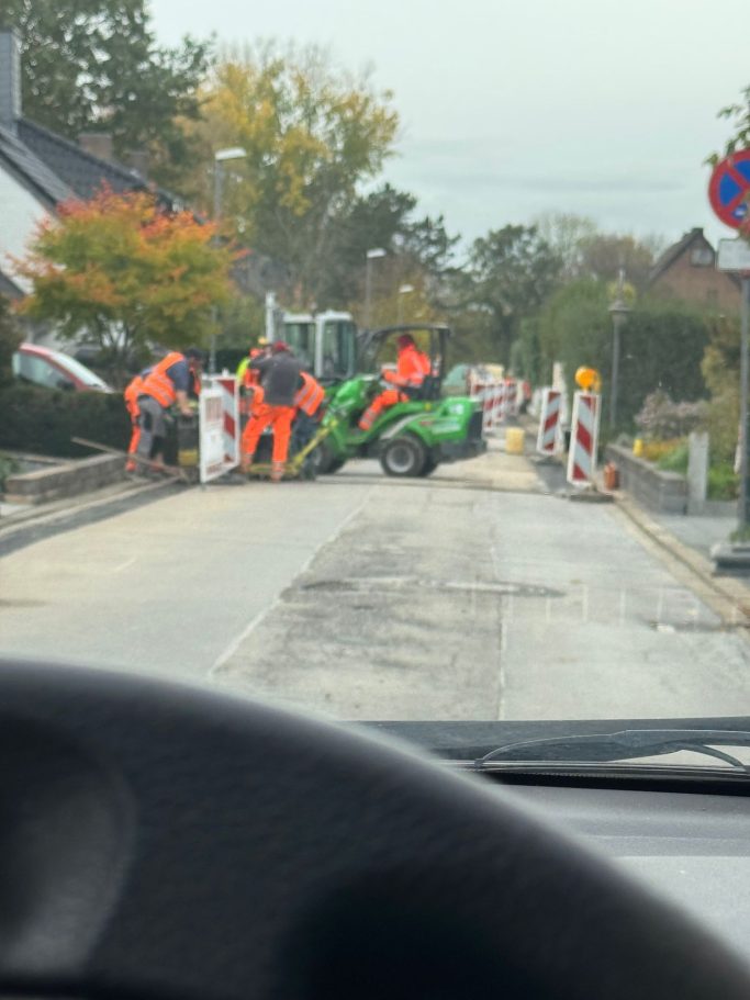 Bauarbeiten auf der Straße mit Bauarbeitern in orangefarbener Kleidung und Baumaschinen.